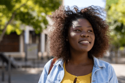 A young African woman with curly hair smiling outdoors on a sunny day, representing lifestyle and community news in Ankole.