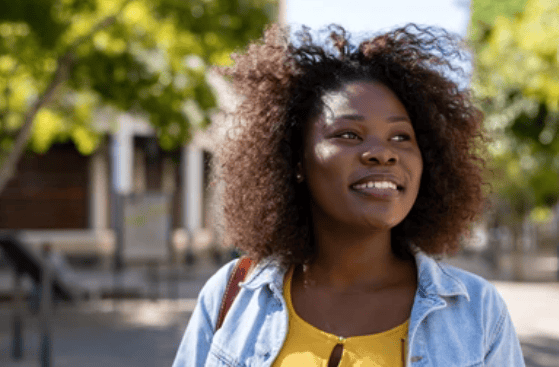 A young African woman with curly hair smiling outdoors on a sunny day, representing lifestyle and community news in Ankole.